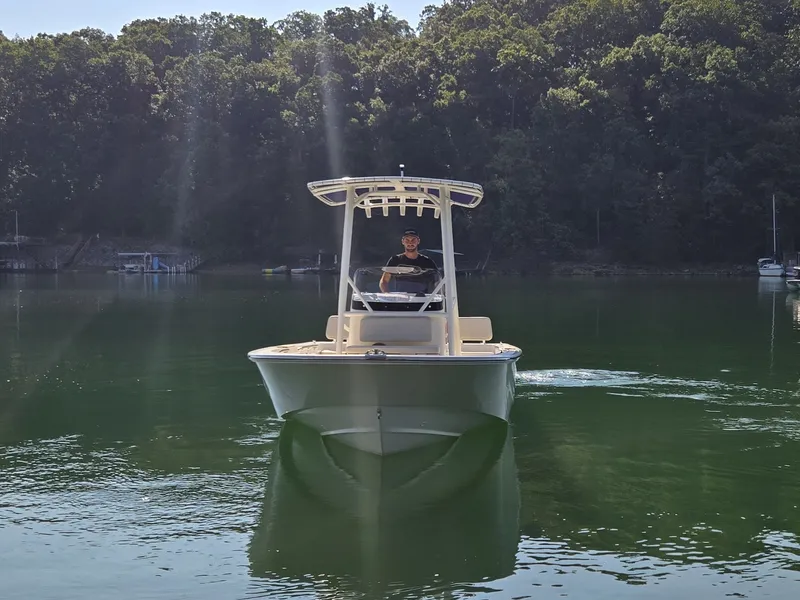 Slide: The Image of A 2026 Boston Whaler 190 Montauk cruising on a calm lake with wooded shores. - 2