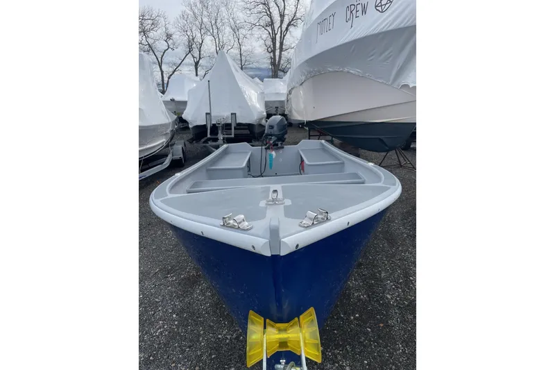Slide: The Image of 2026 Holland 14 boat in storage, blue hull, parked among covered boats. - 2