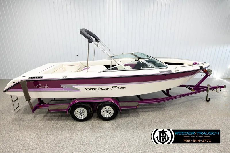 The Image of 1993 American Skier Eagle boat with purple accents on a matching trailer in a showroom. - 1