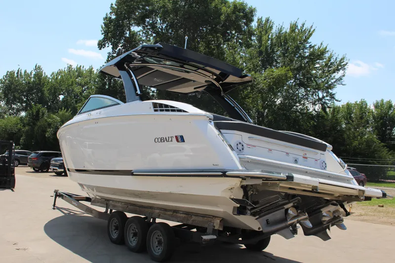 Slide: The Image of 2025 Cobalt R33 Surf boat on trailer, parked outdoors with trees in background. - 11