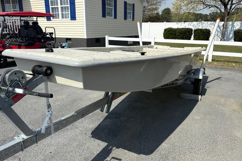 Slide: The Image of 2025 Coastal Skiff 145 boat on trailer, parked near a house with blue shutters. - 2