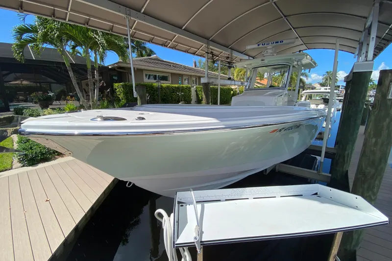 Slide: The Image of 2015 Edgewater 320CC boat docked under a canopy, surrounded by lush greenery. - 1