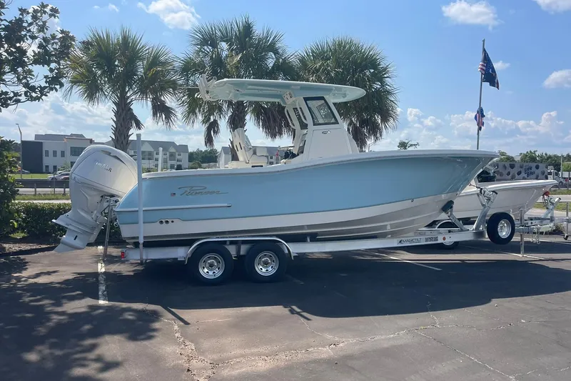 The Image of 2026 Pioneer 250 Pelagic boat on trailer, parked under palm trees, clear sky background. - 0