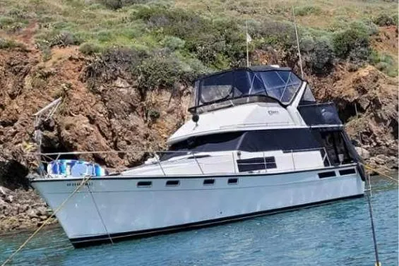 The Image of 1986 Bayliner 3870 Motoryacht anchored near rocky shoreline. - 1