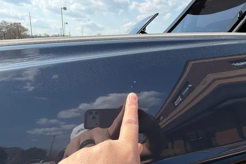 Slide: The Image of Close-up of a 2023 Supra SL 550 with a finger pointing at paint imperfections. - 11