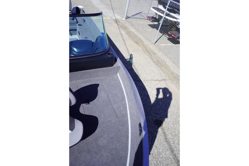 Slide: The Image of 2026 Lowe Fishing Machine 1775WT boat deck with windshield, parked near a chain-link fence. - 16