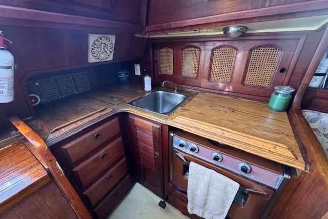 Slide: The Image of 1977 Islander 32 yacht kitchen with wooden cabinetry, sink, stove, and fire extinguisher. - 14
