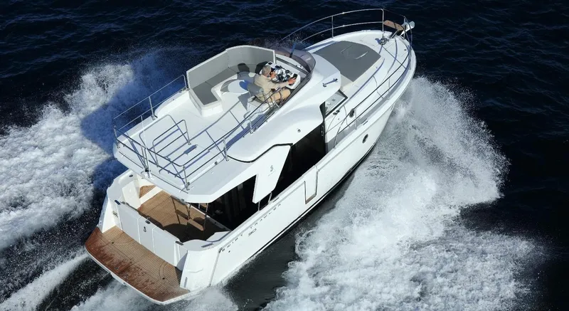 Slide: The Image of Manufacturer Provided Image: 2020 Beneteau Swift Trawler 30 cruising on open blue sea near rocky coastline. - 14