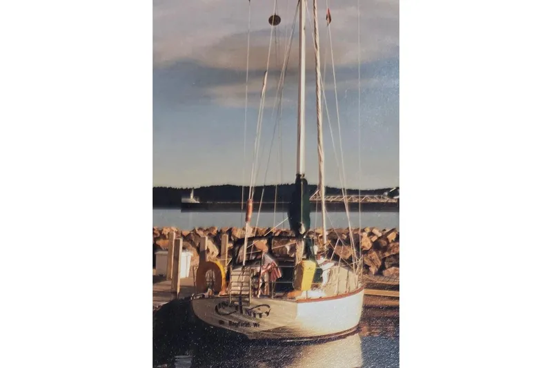 Slide: The Image of 1980 Cape Dory 33 sailboat docked at a serene marina with rocky shoreline. - 5