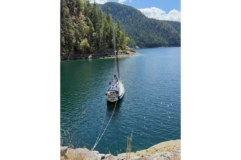 Slide: The Image of Sailboat Cabo Rico 38R, 1990, anchored in a serene, forested bay. - 38