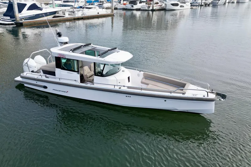 Slide: The Image of 2023 Axopar 28 Cabin boat docked in a marina, surrounded by other vessels. - 13