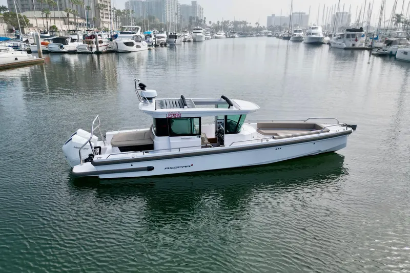 Slide: The Image of 2023 Axopar 28 Cabin boat docked in a marina with surrounding yachts. - 15