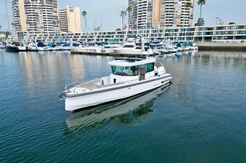 Slide: The Image of 2023 Axopar 28 Cabin boat in marina with modern buildings in background. - 2
