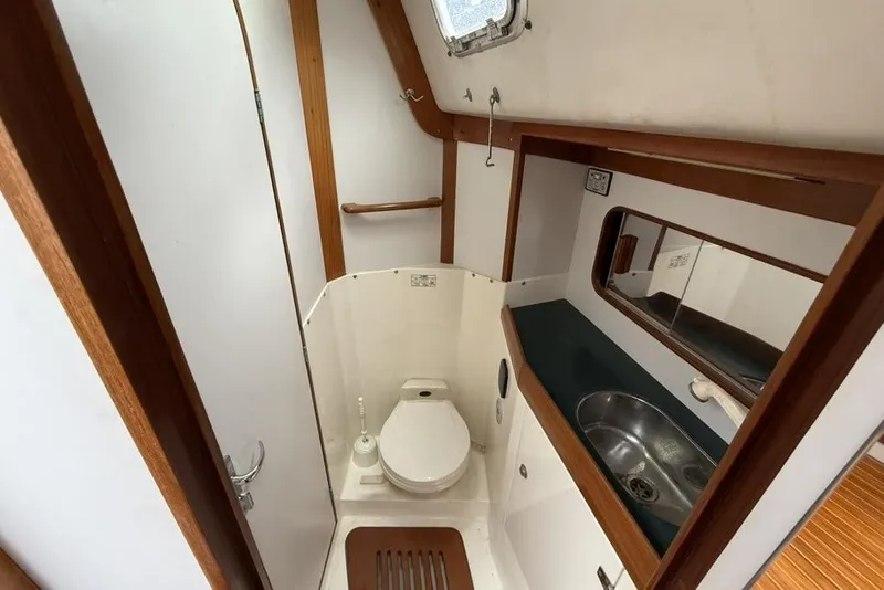 Slide: The Image of 1996 J Boats J/160 yacht bathroom with toilet, sink, mirror, and wooden accents. - 23