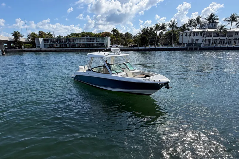Slide: The Image of 2021 Boston Whaler 280 Vantage boat on calm water, with palm trees and buildings in the background. - 33