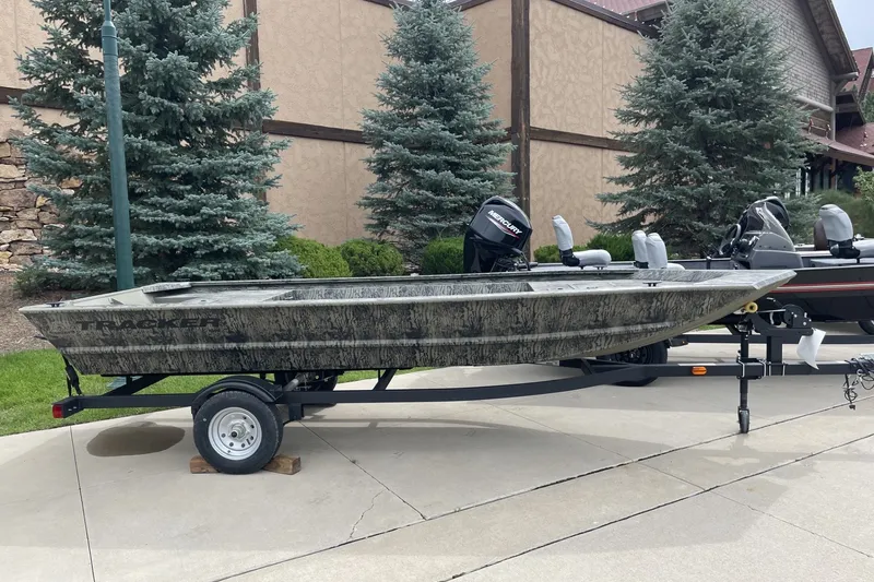 The Image of 2026 Tracker Grizzly 1648 Utility boat on trailer, parked outdoors near trees. - 0
