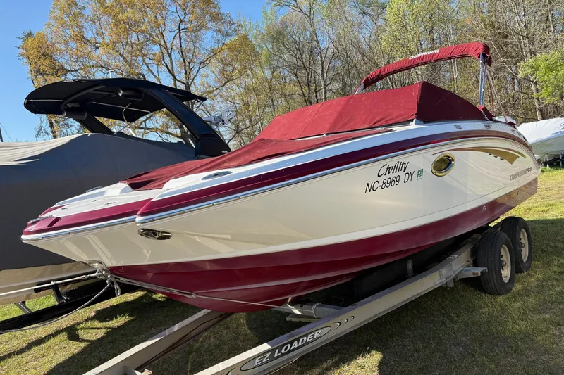 The Image of 2013 Chaparral 244 Sunesta boat with red cover on trailer, surrounded by trees. - 0