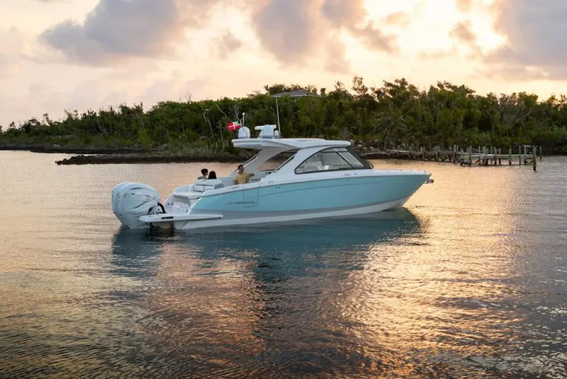 Slide: The Image of Manufacturer Provided Image: 2026 Regal LX36 boat on calm water at sunset, with lush greenery in the background. - 2