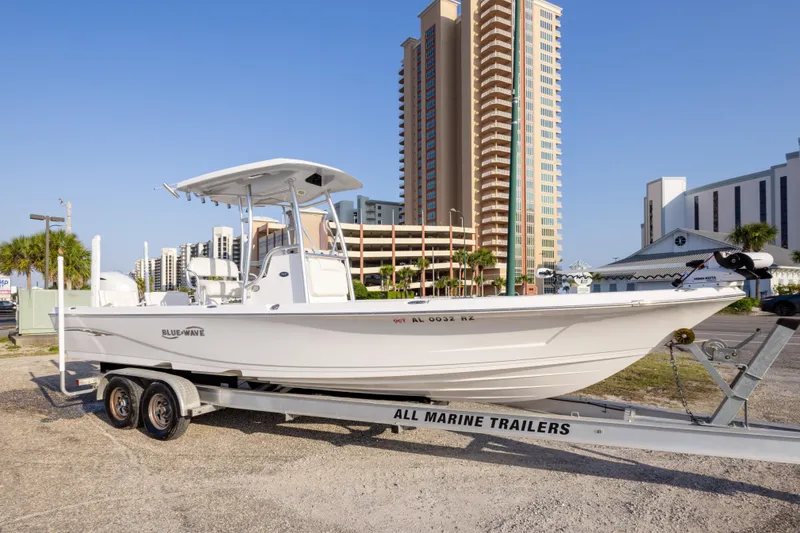 Slide: The Image of 2021 Blue Wave 2600 PureBay boat on trailer, urban backdrop, clear sky. - 2
