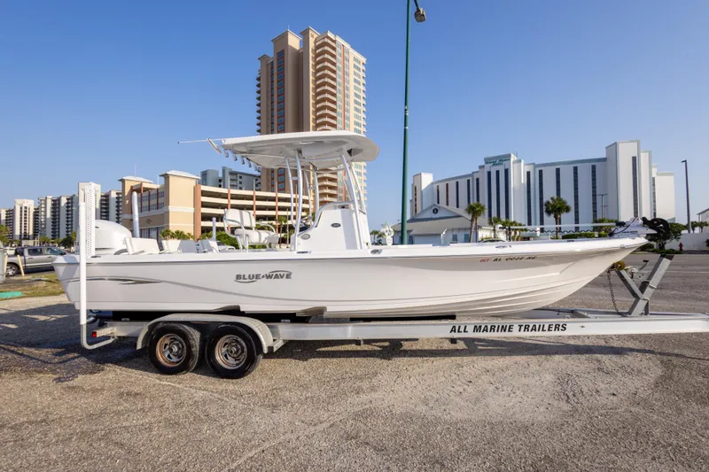 Slide: The Image of 2021 Blue Wave 2600 PureBay boat on trailer, urban backdrop, clear sky. - 4