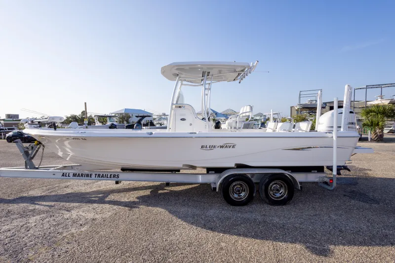 Slide: The Image of 2021 Blue Wave 2600 PureBay boat on trailer, side view, in a marina setting. - 8
