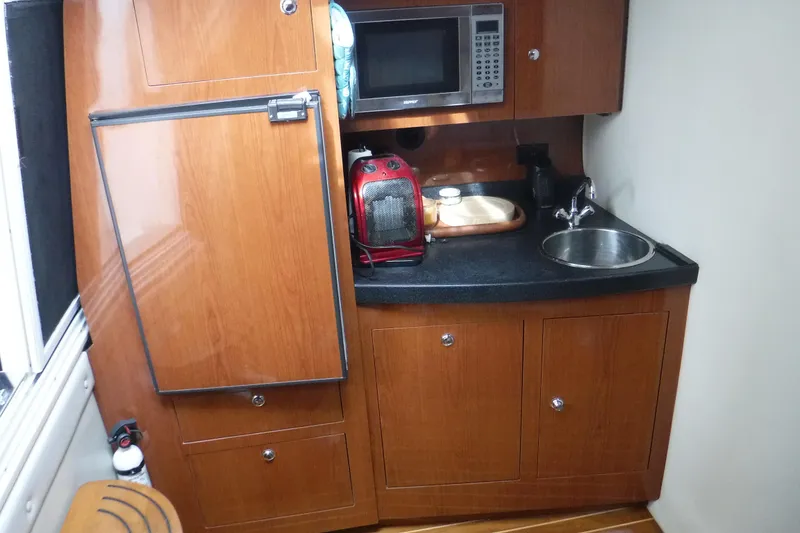 Slide: The Image of Compact kitchen area in a 2006 Regal Commodore 3560 IO boat, featuring wood cabinetry and appliances. - 13