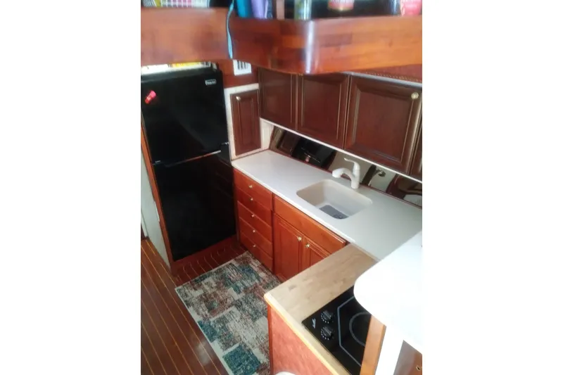 Slide: The Image of 1976 Viking 40 Sedan Diesel yacht kitchen with wooden cabinets, sink, and black refrigerator. - 16