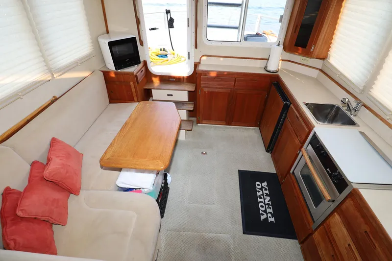 Slide: The Image of Interior of 2007 Nordic Tug 32, featuring cozy seating, kitchenette, and wooden cabinetry. - 4