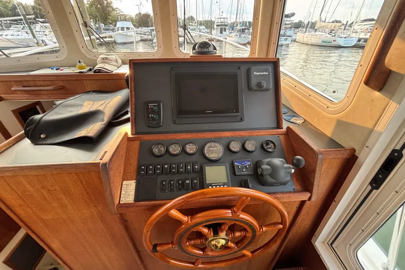 Slide: The Image of 2007 Nordic Tug 32 helm with wooden wheel, navigation instruments, and marina view. - 8