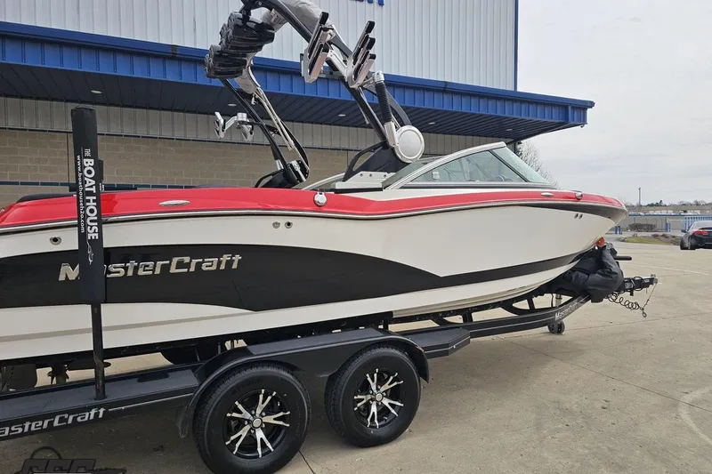 Slide: The Image of 2013 MasterCraft X-10 boat on trailer, red and white design, parked outside a building. - 11