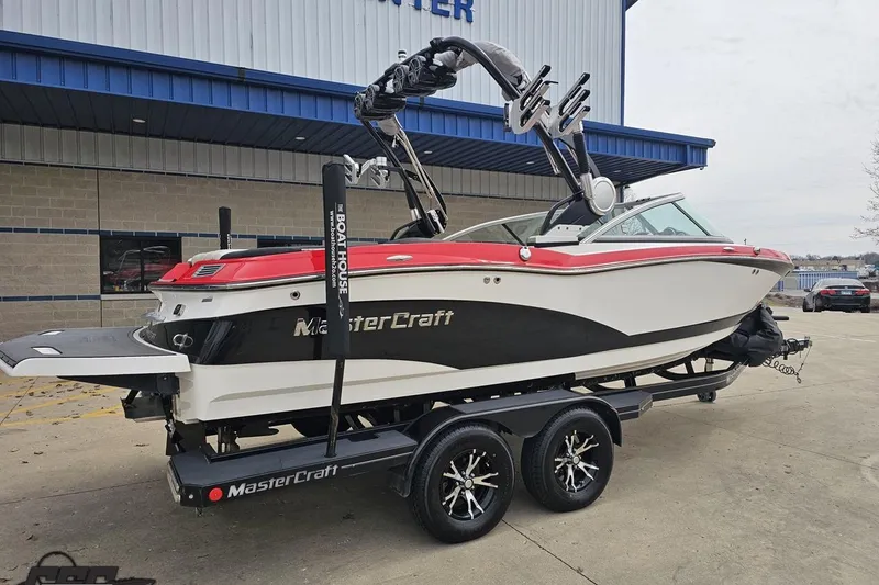 Slide: The Image of 2013 MasterCraft X-10 boat on trailer, red and white design, parked outside a building. - 12