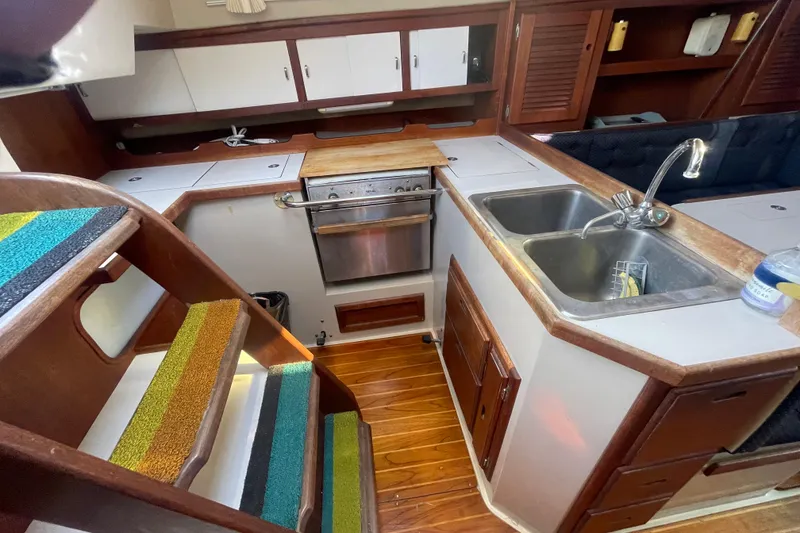 Slide: The Image of 1989 Catalina 36 yacht interior kitchen with wooden cabinetry, dual sink, and colorful stair treads. - 10