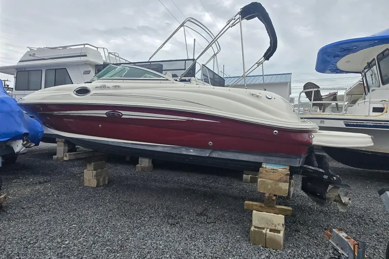 Slide: The Image of 2007 Sea Ray 240 Sundeck boat on blocks, red and white hull, overcast sky. - 4