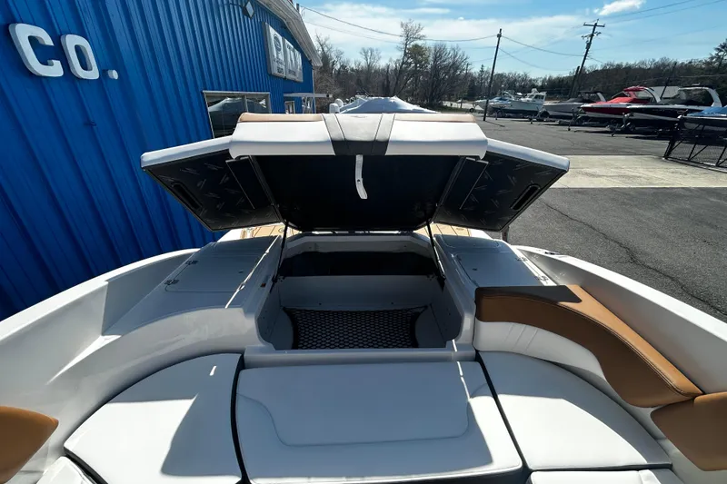 Slide: The Image of 2026 Chaparral 23 SSi OB boat with open storage compartment, docked near blue building. - 23