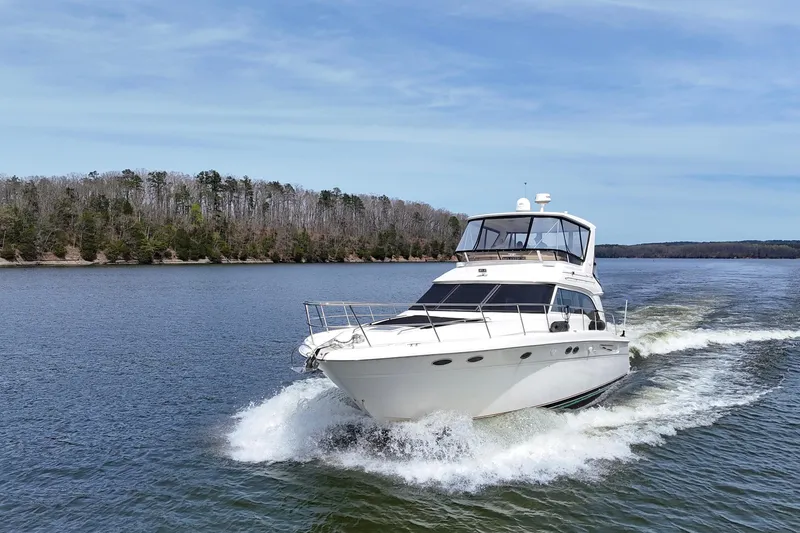 Slide: The Image of 1999 Sea Ray 480 Sedan Bridge cruising on a serene lake with forested shoreline. - 14