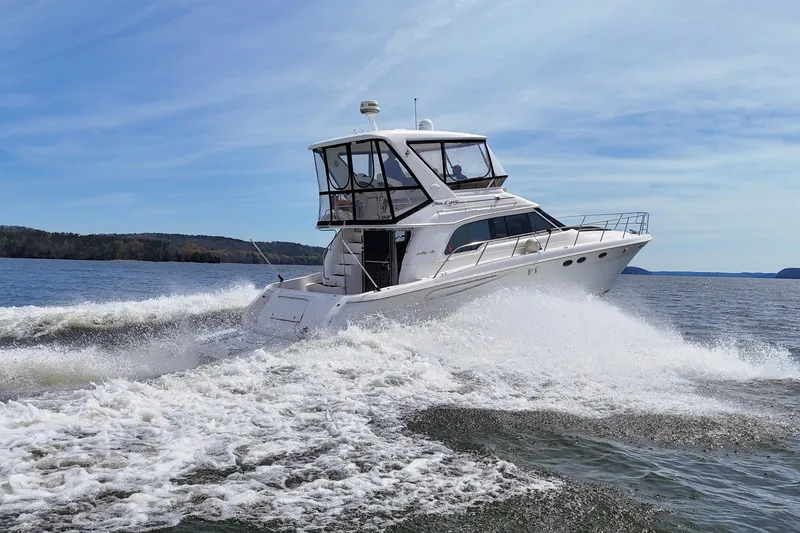 Slide: The Image of 1999 Sea Ray 480 Sedan Bridge cruising on a scenic lake under a clear blue sky. - 15