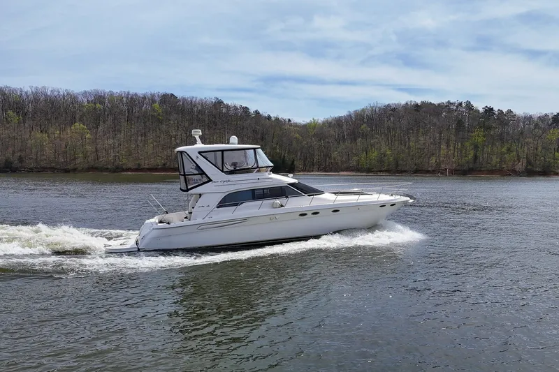 Slide: The Image of 1999 Sea Ray 480 Sedan Bridge cruising on a serene lake with forested shoreline. - 16