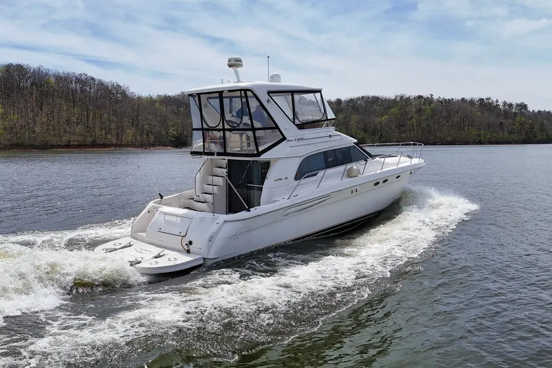 Slide: The Image of 1999 Sea Ray 480 Sedan Bridge cruising on a serene lake with forested shoreline. - 17