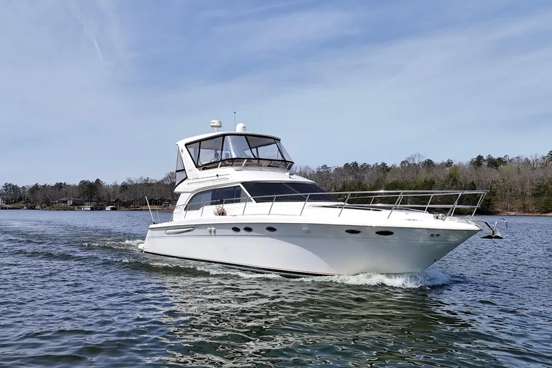 Slide: The Image of 1999 Sea Ray 480 Sedan Bridge yacht cruising on a serene lake under a clear sky. - 2