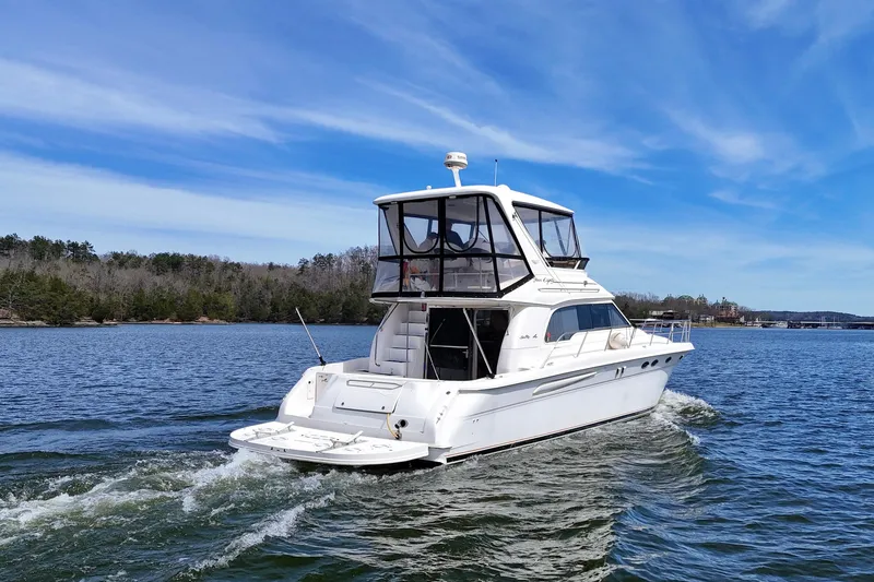 Slide: The Image of 1999 Sea Ray 480 Sedan Bridge yacht cruising on a serene lake under a clear blue sky. - 3
