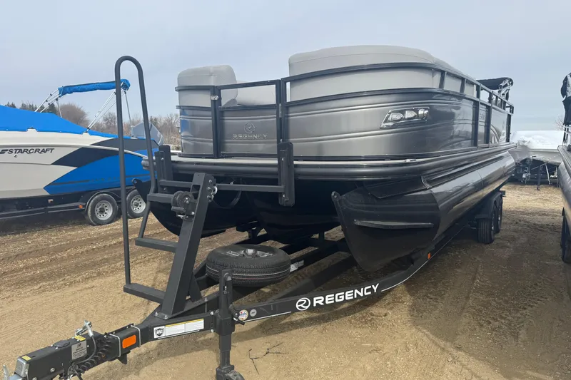 Slide: The Image of 2024 Regency 250 DL3 pontoon boat on trailer, parked outdoors. - 1