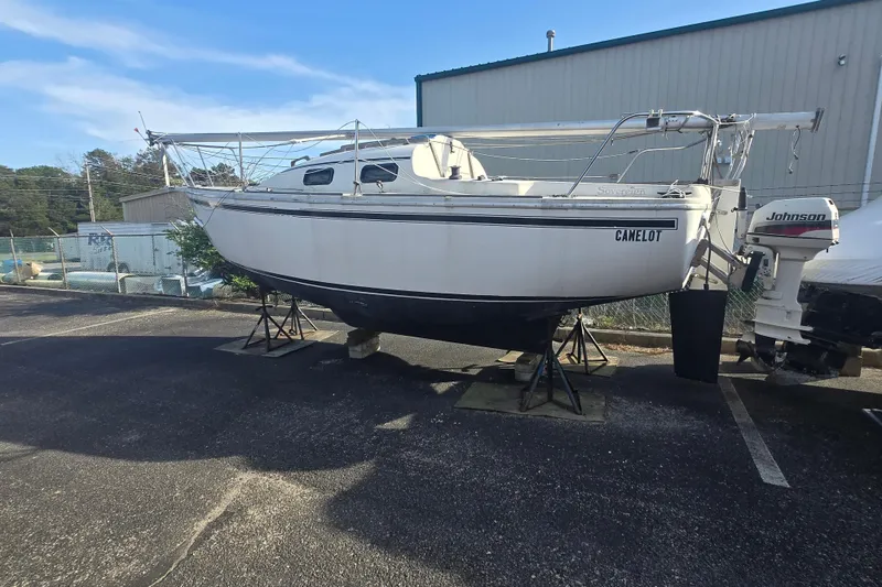 Slide: The Image of 1986 Sovereign 24 sailboat on stands, with Johnson outboard motor, parked outdoors. - 24