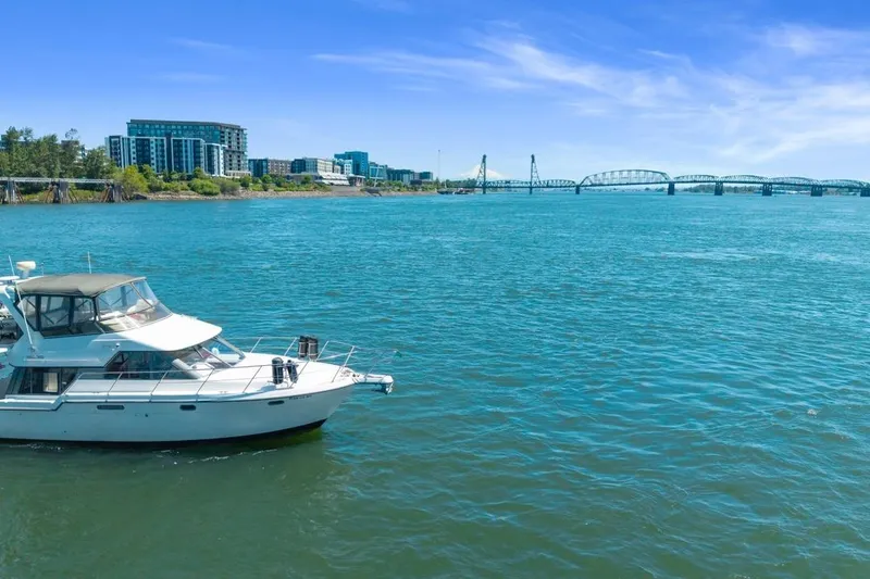 Slide: The Image of 1994 Carver 370 Voyager yacht cruising on a scenic river with cityscape and bridge in background. - 66