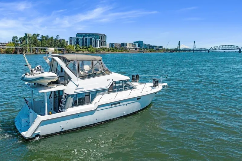Slide: The Image of 1994 Carver 370 Voyager yacht cruising on a scenic river with cityscape and bridge backdrop. - 71