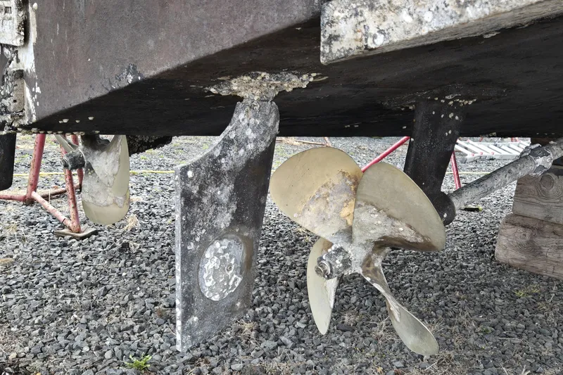 Slide: The Image of 1998 Wellcraft 330 Coastal boat propellers and rudders on gravel, showing wear and marine growth. - 27