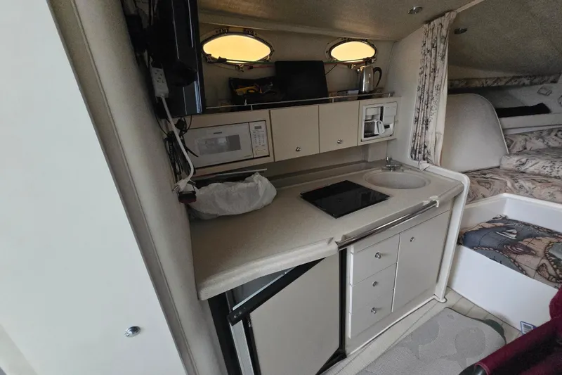 Slide: The Image of 1998 Wellcraft 330 Coastal interior with kitchenette, featuring sink, stove, microwave, and cozy sleeping area. - 6
