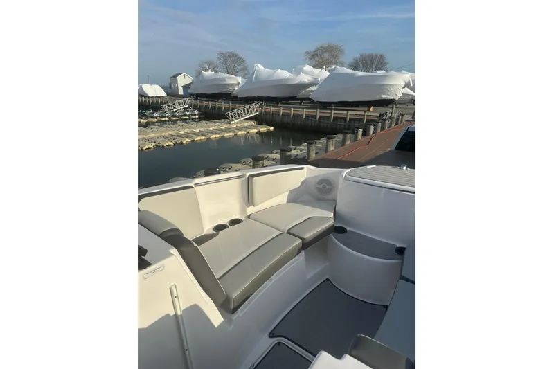 Slide: The Image of 2025 Yamaha Boats AR220 interior with gray seating, docked near covered boats. - 21