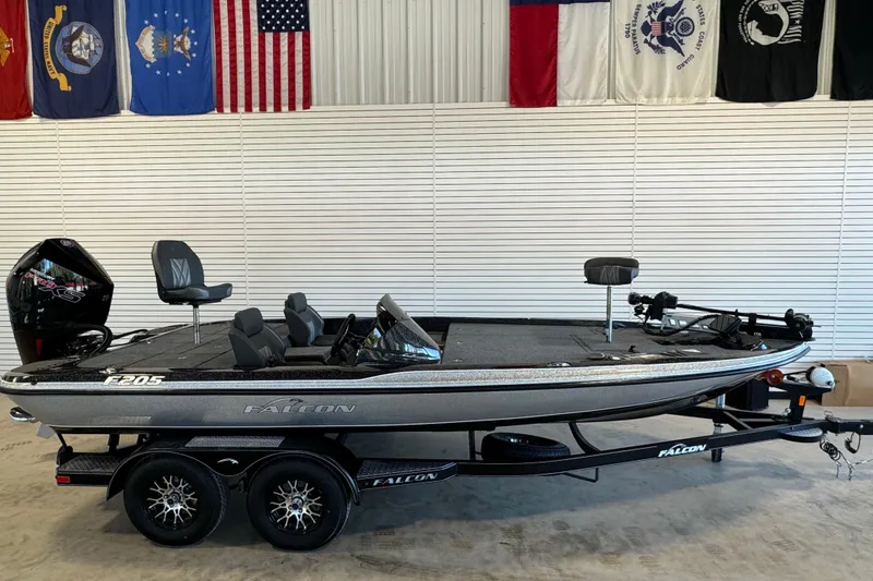 The Image of 2025 Falcon Boats F205 fishing boat on trailer, displayed indoors with flags above. - 1