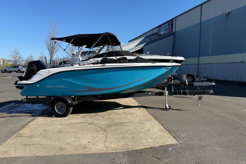 The Image of 2024 Bayliner Element M19 boat on trailer, parked outdoors near industrial building. - 0