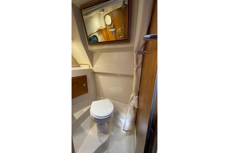 Slide: The Image of 2025 Ranger Tugs R-27 Seakeeper Ride bathroom with toilet, mirror, and wooden accents. - 35